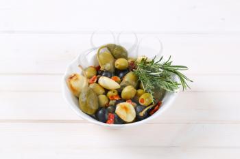bowl of pickled olives, capers, caper berries and garlic on white wooden background