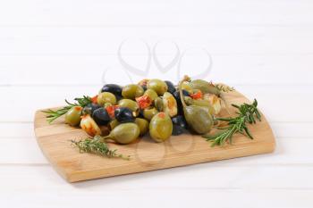 pile of pickled olives, capers, caper berries and garlic on wooden cutting board