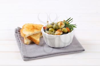 bowl of pickled olives, capers and caper berries served with toast