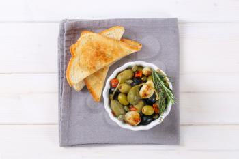 bowl of pickled olives, capers and caper berries served with toast