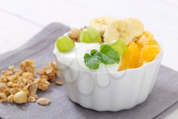 bowl of muesli with yogurt and fresh fruit on grey place mat - close up