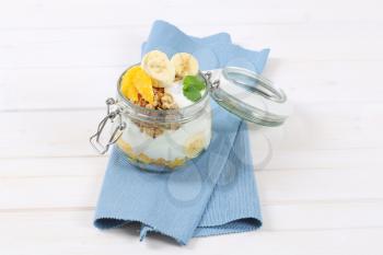 jar of muesli with yogurt and fresh fruit on blue place mat