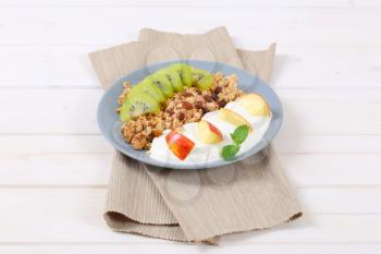 plate of muesli with yogurt and fresh fruit on beige place mat