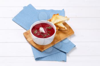 bowl of beetroot cream soup with toast on wooden cutting board