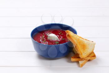 bowl of beetroot cream soup with toast on white wooden background