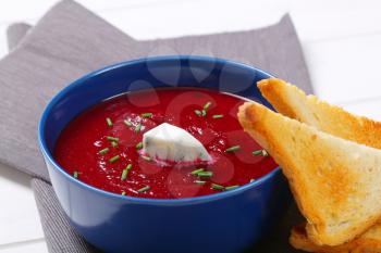 bowl of beetroot cream soup with toast on grey place mat - close up