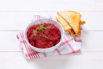 bowl of fresh beetroot puree with toast on checkered dishtowel