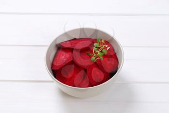 bowl of thin beetroot slices on white wooden background