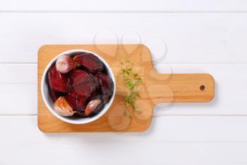 bowl of baked beetroot with garlic and thyme on wooden cutting board