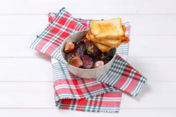 bowl of baked beetroot and garlic with toasted bread on checkered dishtowel