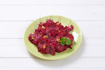 plate of fresh beetroot spread with walnuts on white wooden background