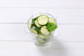 glass of green zucchini slices on white wooden background