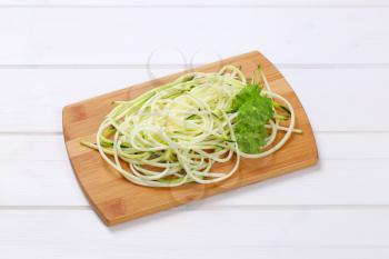 heap of raw zucchini noodles on wooden cutting board