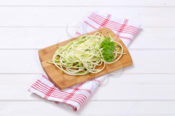 heap of raw zucchini noodles on wooden cutting board
