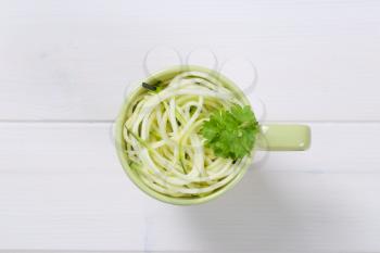 cup of raw zucchini noodles on white wooden background