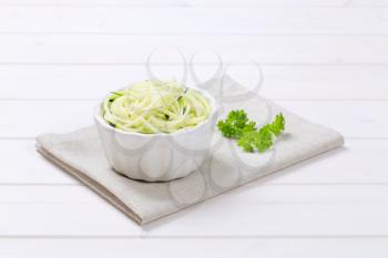 bowl of raw zucchini noodles on beige place mat