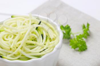 bowl of raw zucchini noodles on beige place mat - close up