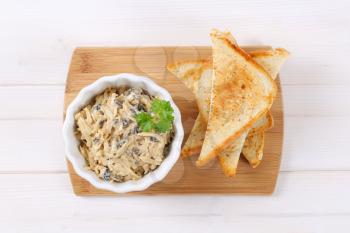 bowl of grated cheese spread with olives and toast on wooden cutting board