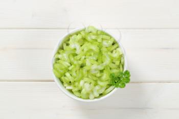 bowl of chopped celery stems on white wooden background