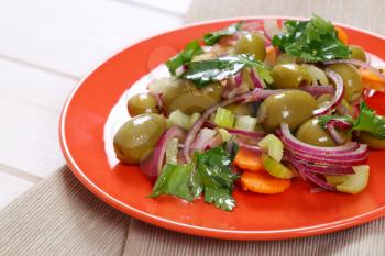 plate of vegetable salad with pickled green olives on beige place mat - close up