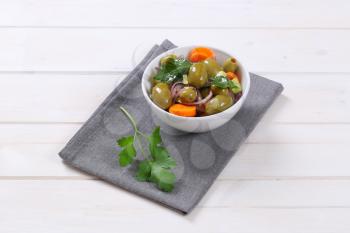 bowl of vegetable salad with pickled green olives on grey place mat