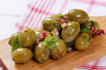 pile of marinated green olives on wooden cutting board - close up