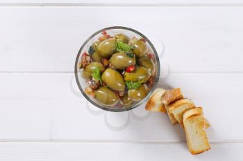glass of marinated green olives with toast on white wooden background