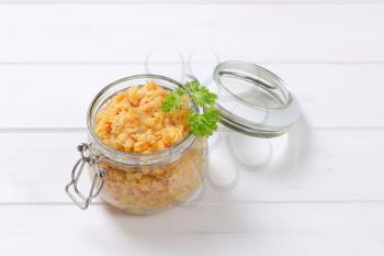 Cooked red lentils in a jar on white wooden background