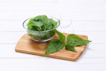 bowl of fresh nettle leaves on wooden cutting board