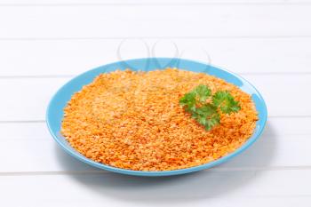 plate of split red lentils on white wooden background