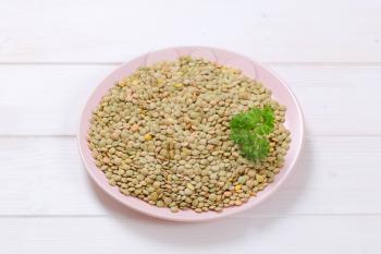 plate of dry brown lentils on white wooden background
