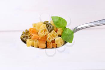 spoon of raw colored pasta on white wooden background
