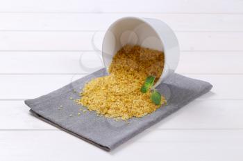 bowl of dry wheat bulgur spilt out on grey place mat