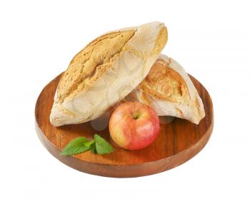 two diamond shaped rustic bread rolls and fresh apple on round wooden cutting board
