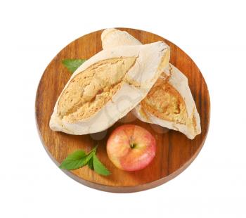 two diamond shaped rustic bread rolls and fresh apple on round wooden cutting board