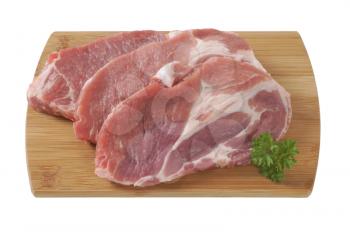 three raw pork neck chops  on wooden cutting board