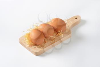 brown eggs and straw on wooden cutting board