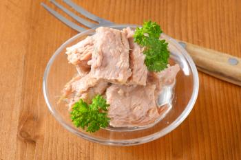 bowl of canned tuna with parsley on wooden table