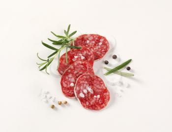 slices of French dry cured salami with spices on white background