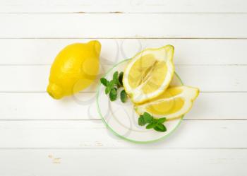 whole and sliced lemons on white plate and wooden background