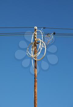 Tangled wires on rusty power pole against blue sky