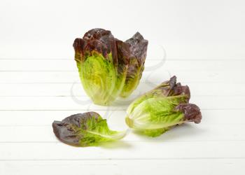 two and half heads of fresh lettuce on white wooden background