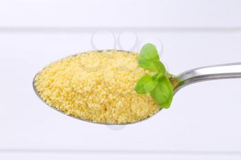 spoon of raw couscous on white wooden background