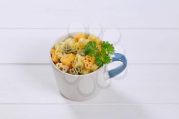 mug of cooked colored pasta on white wooden background