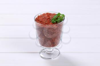 glass of red rice on white wooden background