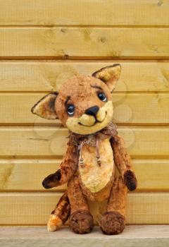Ron fox cub on the background of a wooden plank wall. Handmade, the sewed plush toy