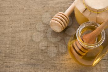 jar and pot of honey with stick on wood background