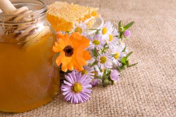 honeycomb, flowers and honey in pot on sacking
