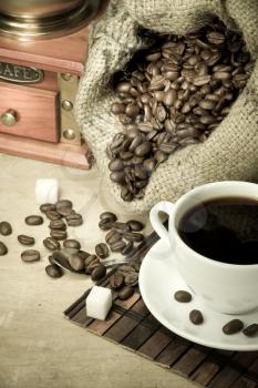 cup of coffee and grinder with roasted beans on wooden background