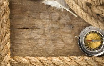 ship ropes and compass with feather at old wooden background
